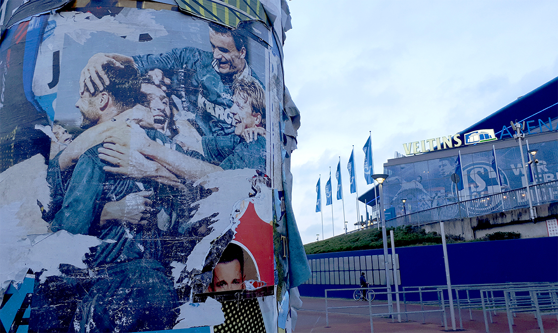 Eine Litfaßsäule mit dem alten Plakat der »Eurofighter« von 1997 vor dem Stadion auf Schalke, oben Martin Max. Außerdem: Youri Mulders, Marc Wilmots, Johan de Kock und Olaf Thon. Foto: © Jan Mohnhaupt